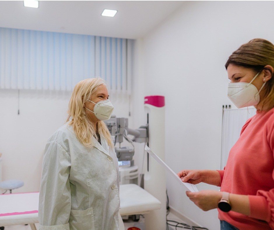 Masked female patient talking with masked female doctor.